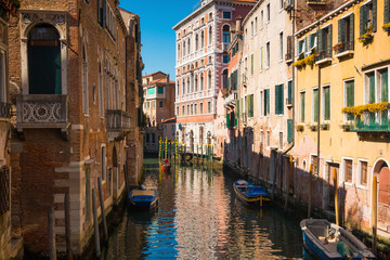 Fototapeta na wymiar Narrow street with a canal, bridge, boats and tourists in Venice