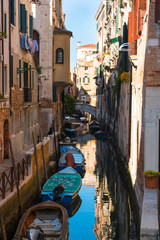 Fototapeta na wymiar Narrow street with a canal, bridge, boats in Venice