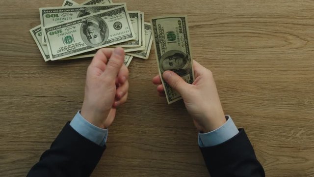 Business man counting cash payment dollars banknotes and give it to someone. Top view.