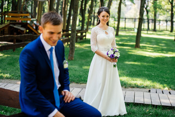 Beautiful young bride with wedding bouquet with groom in blur in front of her. Wedding couple in love at wedding day