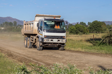 Construction truck moving fast with load of rock and sand on dirt road