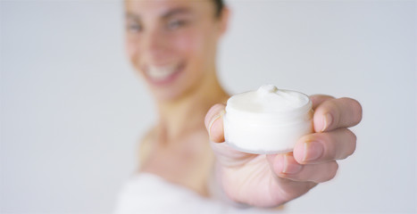 Portrait of a beautiful young girl smiling and looking at the camera, without makeup, holding cream, on a white background. Concept:natural beauty, youth, skin care, always young, love yourself.