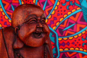 Obraz premium Buddha statue on a colorful background / featuring a wooden statue of cheerful wise Buddha on colorful Oriental artistic pattern background