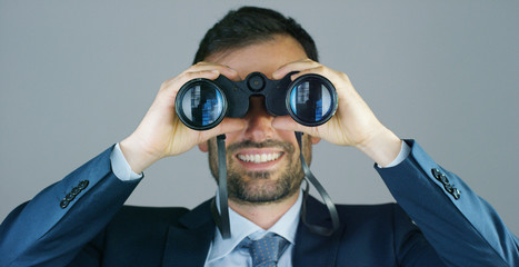A businessman in a suit and tie, use the binoculars to look away with the concept of looking to the...
