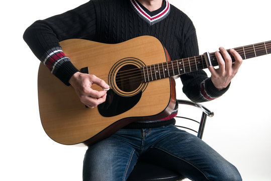 A guitarist in jeans and a black sweater plays an acoustic guitar with a slider sitting on a chair in the center of the frame on a white background. Horizontal frame.