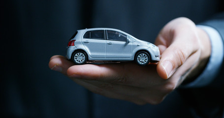 A man dressed in a suit and tie, shows a small auto. Concept: car insurance, mechanical, leasing,...