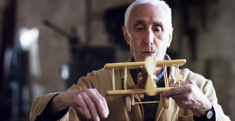 in an old carpentry an elder is working the wood to create a toy airplane with traditional instruments	