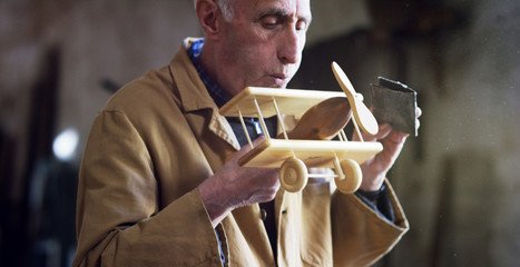 in an old carpentry an elder is working the wood to create a toy airplane with traditional instruments	