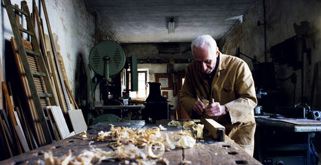 in an old carpentry an elder is working the wood to create a toy airplane with traditional instruments	