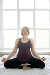 Pregnant woman sitting in lotus pose in bed