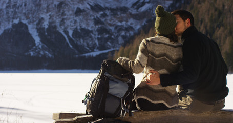 A girl rests and relaxes watching snowy mountains in front of them embraced with boyfriend, lovers embrace after the walk in the snow. Concept: the mountains, relaxation, hiking, love