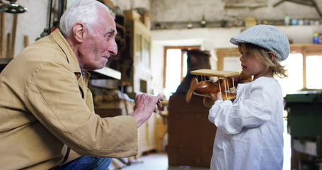 in an old carpentry shop a child and grandfather playing with a wooden airplane concept of tradition that continues over time	