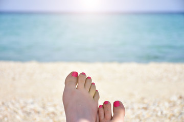 woman's feets with pink nails on the sea shore background