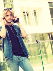 Hipster man standing on city street listening music