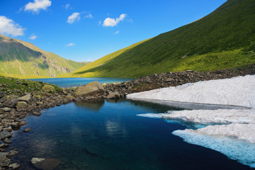 Mountain Lake in the mountains of Western Caucasus. Bright blue sky and white clouds.