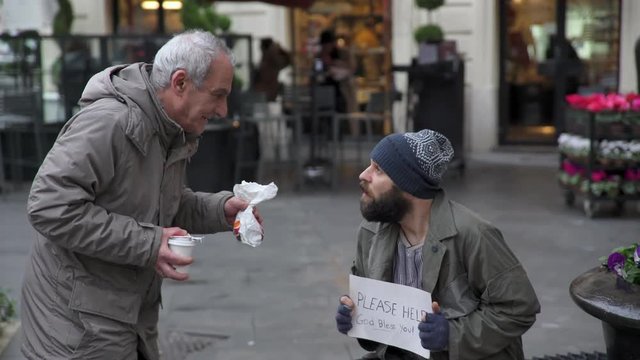 Old and kind man brings breakfast to a beggar sitting in the street