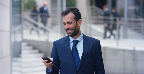 A businessman answering the phone, send messages and smiles for the beautiful job news and in the background you see a skyscraper. Concept: technology, telephony, business trips, business, wall street