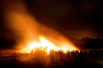 crowd silhouettes surrounding a huge burning Easter bonfire and celebrating as the night sets in the village