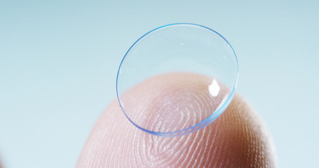 Macro shot of a finger holding a contact lens technology with a chip to see better in both eyes and...