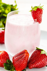 Large ripe strawberries and a glass of drinking yogurt on a light background