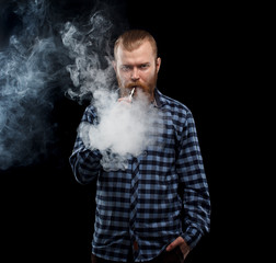 Obraz na płótnie Canvas Vaping man holding a mod. A cloud of vapor. Black background. Studio shooting.