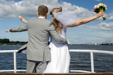 Bride and groom standing in front of the yacht in the wind.