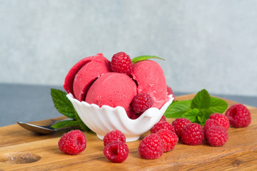 Raspberry ice cream sorbet in white porcelaine bowl with raspberry, mint leaves  copy space on wooden plank and grey textured background