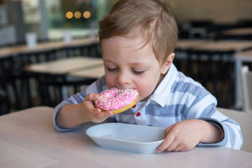 Cute baby boy eating sweet donut in cafe