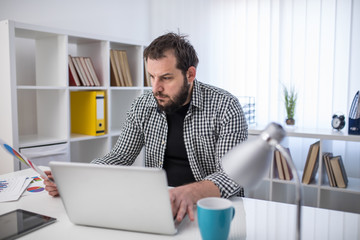 Naklejka premium Handsome bearded businessman working with laptop in office