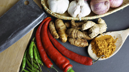 Asian cuisine ingredients of herbs, spices, turmeric, red pepper, green pepper, knife, garlic and shallots. on a black background. View from the Top
