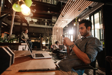 Handsome young man sitting at office cafe using phone