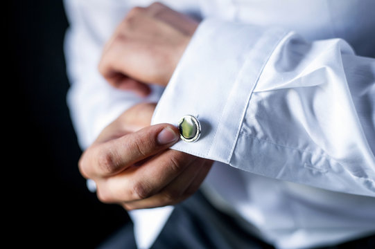 A man adjusts his cuff on a white shirt.