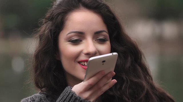 Beautiful girl registers voice message on smartphone,outdoors