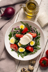 Italian salad prepared with arugula, mozzarella, eggs. white wooden background