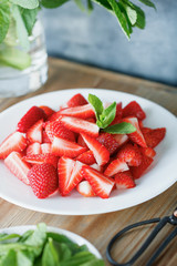 Freshly sliced strawberry with peppermint on a white plate on a wooden table. Healthy food concept.