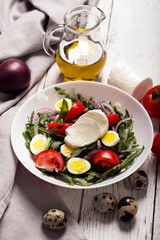 Obraz na płótnie Canvas Italian salad prepared with arugula, mozzarella, eggs. white wooden background