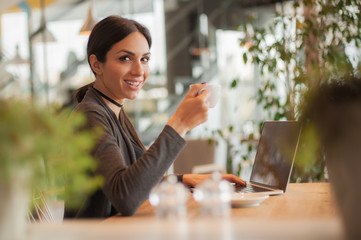 Smiling young woman drinking a coffee and surfing on internet