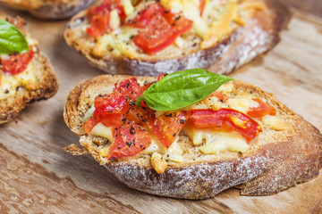 Italian bruschetta with roasted tomatoes, mozzarella cheese and herbs on a cutting board