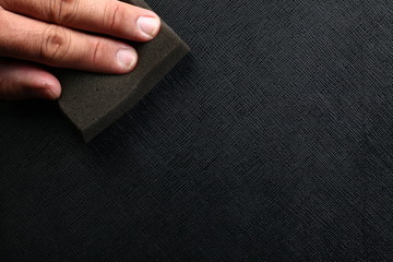 Man hand in action of leather polishing with sponge on black leather.