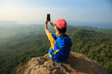 successful woman hiker taking photo with smartphone on mountain peak cliff