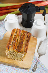 Coconut and rhubarb cake. White wooden table, dark blue plates, silver cutlery. 