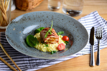 Juicy chicken roll with risotto, cherry tomatoes and greenery on a plate served for a dinner in a restaurant. Tasty food concept.