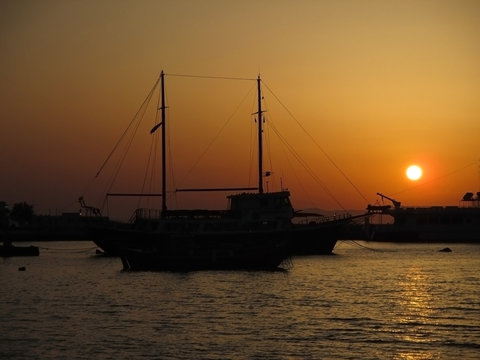 Silhouette of sailboat against the stunning sunset over the Old Port of Mykonos, Greece 