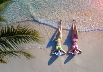women in bikini enjoy on the beach by laying down on the sand under coconut tree palm with swell of...