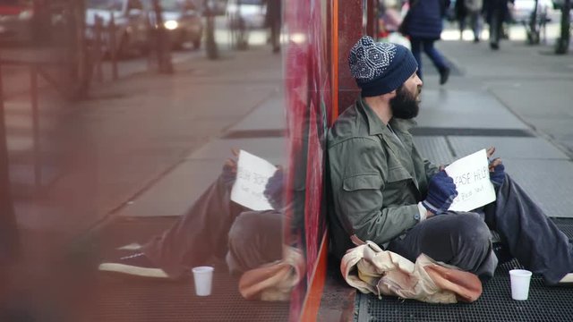 A homeless person sitting alone on the street asks for alms 