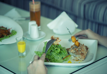 Fish with a salad in a plate is servered on a table with a glass of carrot juice. The female is having lunch.