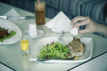 Fish with a salad in a plate is servered on a table with a glass of carrot juice. The female is having lunch.