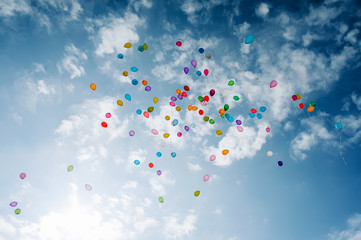 a lot of multicolored balloons in a blue sky with clouds.