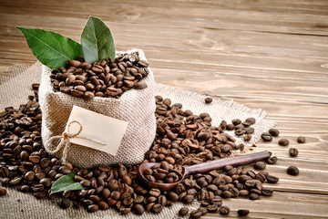 Bag of burlap filled with coffee beans on wooden background.