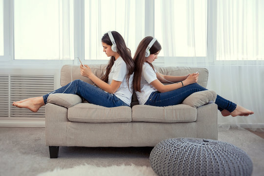 Sisters teenage girls with smart phone and headphones listening music and ommunicate in social networks